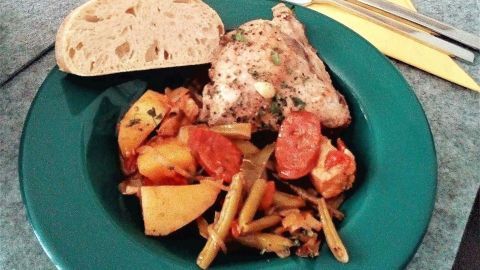 Ein Teller Cataplana de Frango zeigt saftiges Hühnchen mit buntem Gemüse und frischem Brot, angerichtet auf einem Tisch.