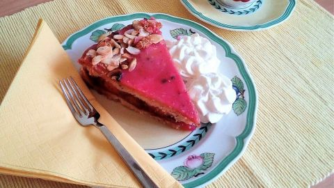 Ein Stück gedeckter Pflaumenkuchen liegt auf einem Teller mit Sahne und einer Gabel, während eine Tasse daneben steht.