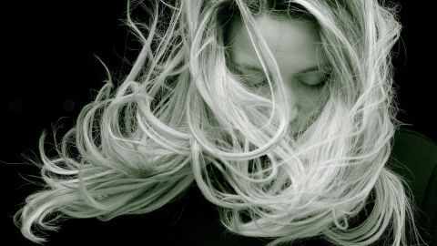Eine Frau mit langen Haaren bewegt ihren Kopf, während ihre Haare im Wind wehen, was Haarausfall und Vitaminmangel symbolisiert.