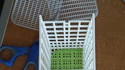 Ein weißer Besteckkorb mit grünem Boden steht auf einem Tisch, während daneben eine Schere liegt, bereit zur Reparatur.