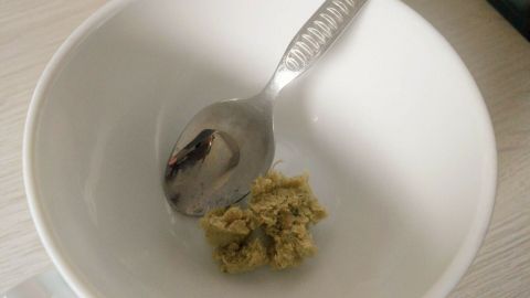 Eine silberne Löffelruht in einer weißen Schüssel, die etwas Hühnerbrühpaste enthält, auf einem hellen Tisch.