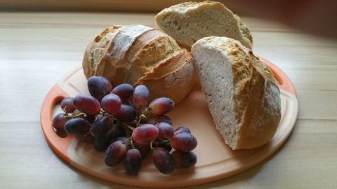 Rustikale Weißbrote liegen auf einem Holzbrett, während Trauben daneben platziert sind, was eine einladende Anrichte ergibt.