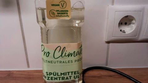 Eine Flasche umweltfreundliches Spülmittel steht auf einer Holzoberfläche neben einem Küchenspülbecken in einer modernen Küche.