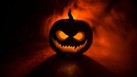 Ein gruselig geschnitzter Kürbis leuchtet in einem orangefarbenen Rauch, der eine gespenstische Halloween-Stimmung erzeugt.