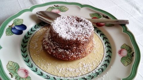 Ein Nougat-Soufflé steht auf einem dekorativen Teller, umgeben von einer feinen Sauce und mit Puderzucker bestäubt.