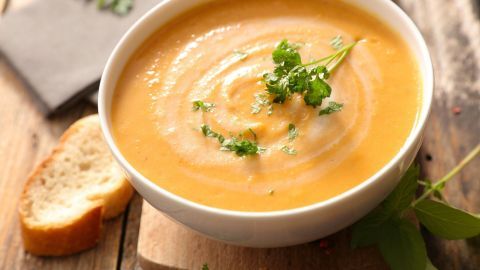 Eine cremige Kürbis-Kohlrabi-Kartoffel-Suppe in einer Schüssel, garniert mit frischem Koriander und serviert mit Brot.