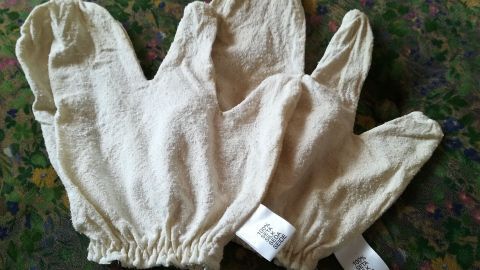 Seidenhandschuhe liegen auf einem bunten Stoff, bereit für eine Massage zur Anregung des Stoffwechsels.