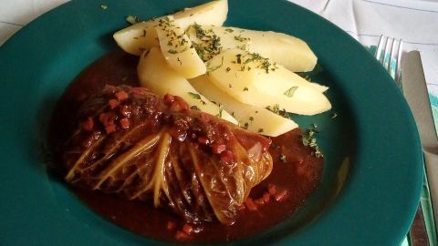Kohlrouladen liegen in einer schmackhaften Sauce auf einem Teller, daneben liegen garnierten Kartoffelstücke.