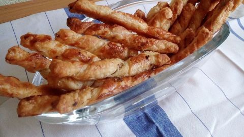 Auf einem Tisch liegen knusprige Blätterteig-Sticks in einer Glasschüssel, schön gebräunt und appetitlich angerichtet.