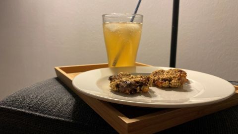 Auf einem Teller liegen zwei Müsli-Kekse mit Schokostückchen, daneben steht ein Glas mit einem gelben Getränk.