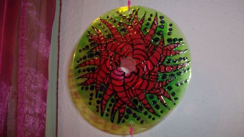 Ein mobiles Element aus einer alten CD, bemalt in leuchtenden Farben, hängt an einer Wand in einem gemütlichen Raum.