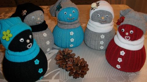 Bunte Socken-Schneemännchen stehen auf einem Tisch, umgeben von einer Tannenzapfen-Deko.