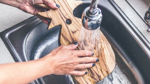 Eine Holz-Schneidbrett wird unter fließendem Wasser im Spülbecken gereinigt, um Gerüche zu entfernen.