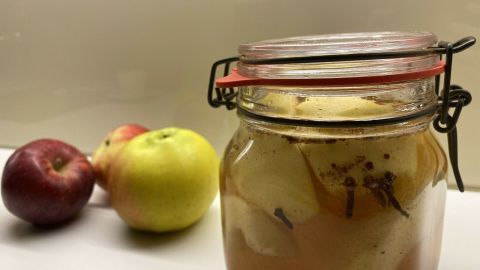 Ein Glas Apfelkompott steht im Vordergrund, umgeben von frischen Äpfeln, die appetitlich und aromatisch wirken.