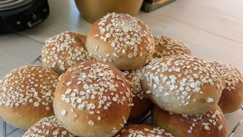 Dinkel-Bananen-Haferflockenbrötchen liegen frisch auf einem Gitter, umgeben von einer grünen Pflanze in der Küche.