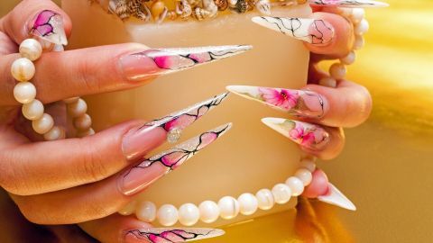 Elegante, lang geschnittene Fingernägel mit buntem Design halten eine dekorierte Kerze in goldener Umgebung.