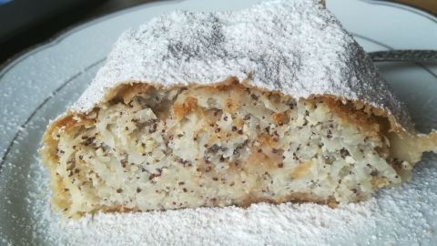 Ein Stück Rübenstrudel liegt auf einem Teller, bedeckt mit Puderzucker und umgeben von einer einfachen Tischoberfläche.