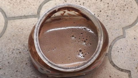 Ein gefüllter Behälter mit schaumigem Nutella-Kakao steht auf einem strukturierten, hellen Untergrund.