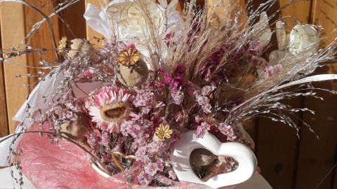 Ein farbenfrohes Herbstgesteck aus Trockenblumen mit rosa Akzenten wird vor einer Holzfläche präsentiert.