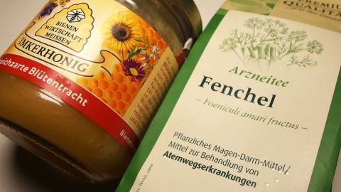"Flüssighonig" aus Fencheltee und festem Honig hilft sehr gut gegen Husten. Ein Glas Honig und eine Packung Fencheltee liegen nebeneinander, bereit zur Linderung von Hustenbeschwerden.