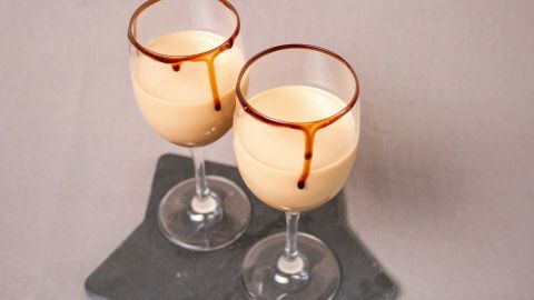 Zwei Gläser mit einem cremigen Cocktail aus Baileys und Amaretto stehen auf einer schwarzen Unterlage und strahlen Genuss aus.