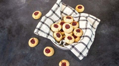 Kleine vegane Spitzbuben liegen in einer Schüssel, umhüllt von einem karierten Geschirrtuch auf einem dunklen Tisch.