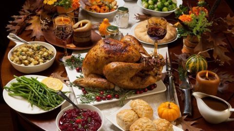 Ein goldbrauner Truthahn liegt auf einem Tisch, umgeben von typischen Thanksgiving-Beilagen wie grünen Bohnen und Cranberrys.
