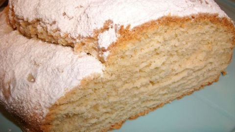 Ein Quarkstollen mit Puderzucker bestäubt liegt auf einem blauen Teller, bereit zum Servieren in einer gemütlichen Küche.