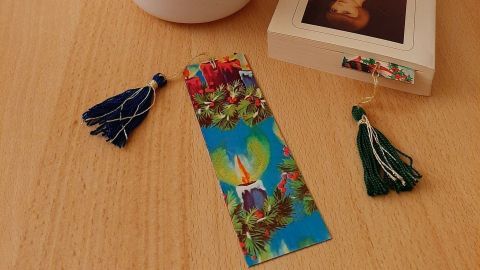 Ein buntes Lesezeichen aus Papierresten liegt neben einem Buch auf einem Holzstisch, umgeben von einer Topfpflanze.