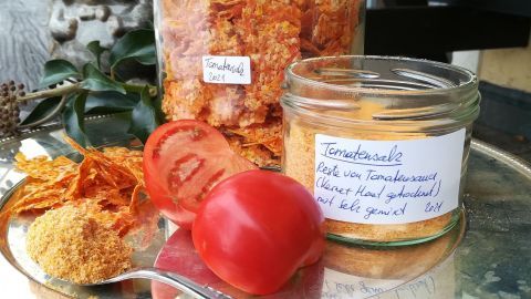 Tomatensalz ist in einem Glas und auf einem Tablett platziert, umgeben von frischen Tomaten und Tomatenresten.