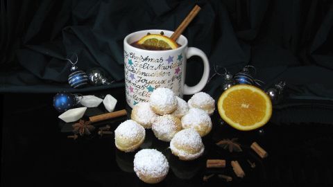 Frischkäse-Schneebällchen liegen neben einem Becher Granatapfel-Punsch mit Zimt und Orange, dekoriert mit weihnachtlichen Accessoires.