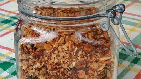 Ein Glas mit knusprigem Granola-Nuss-Müsli steht offen auf einem karierten Tisch, umgeben von einem rustikalen Ambiente.