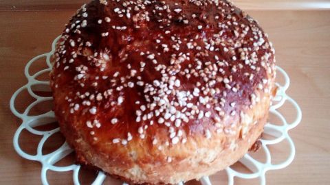 Ein runder Walnuss-Kloben mit goldbrauner Kruste und Sesam oben, auf einem weißen dekorativen Teller in einer Küche.
