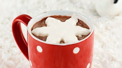 Eine rote Tasse mit Kakao und gefrorener Sahne in Schneeflockenform steht auf weißem, schneebedecktem Untergrund.