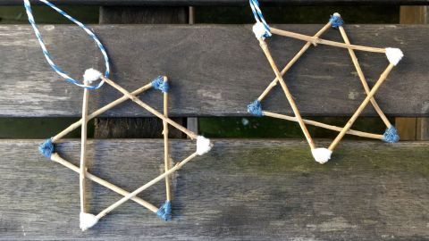 Zwei Weihnachtssterne aus Zweigen liegen auf einem Holzbrett, bunt geknotet und bereit zum Hängen.