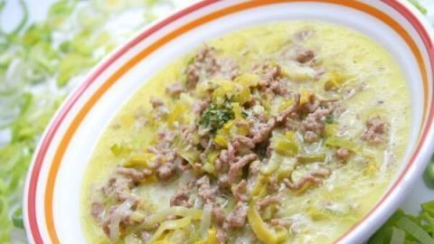 Eine Schüssel Hack-Lauch-Käsesuppe steht auf einem Teller, gekrönt von Hackfleisch und Lauch, in einer hellen, frischen Umgebung.