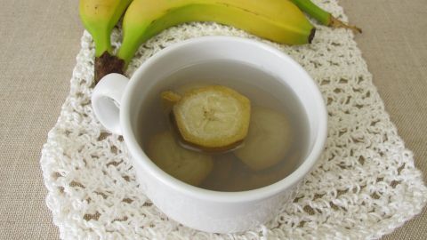 Eine Tasse mit Tee aus Bio-Bananen steht auf einer weißen Unterlage, umgeben von frischen Bananen.