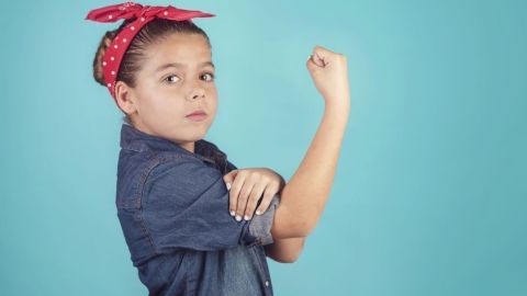 Ein Mädchen mit einem roten Bandana zeigt entschlossen ihren geballten linken Arm vor einem hellblauen Hintergrund.