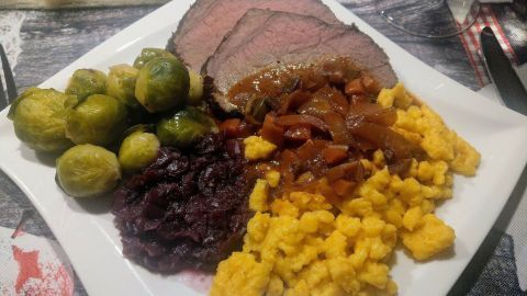 Auf einem Teller liegen saftige Kürbisspätzle, umgeben von Rinderbraten, Rotkohl und Rosenkohl.