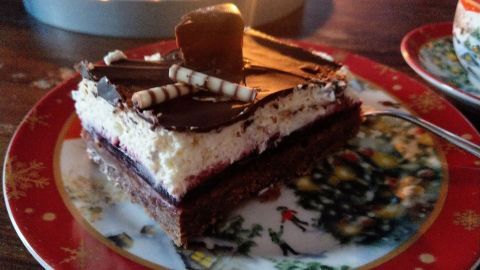 Ein Stück Dominostein-Kuchen liegt auf einem dekorativen Teller mit weihnachtlichem Motiv und einem Löffel daneben.