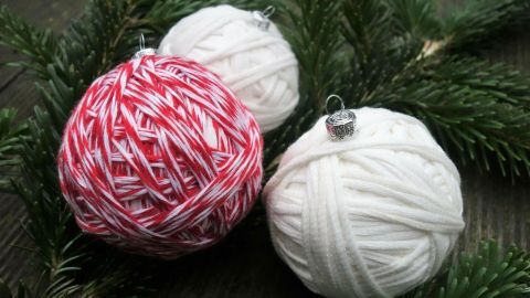 Wolle wird zu festlichen Weihnachtskugeln geformt, die auf einem grünen Zweig liegen. Weihnachtsdekoration in natürlichem Umfeld.