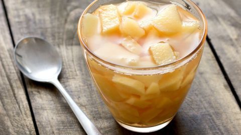 Ein Glas Quitten-Apfel-Kompott mit Sternanis steht auf einer rustikalen Holzoberfläche, neben einem silbernen Löffel.
