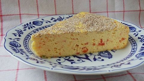 Ein Stück käsekuchen ist auf einem blauen, gemusterten Teller angerichtet. Das Desserts mit Tomaten und Chia-Samen steht vor einem karierter Tischdecke.