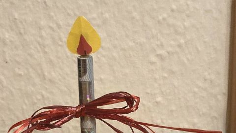 Eine rot bemalte Kerze mit einem Geldschein als Docht ist kunstvoll auf einem Holztisch platziert, um Geldgeschenke zu verpacken.