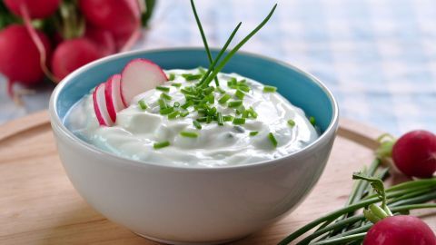 Ein Schälchen mit Radieschen-Schnittlauch-Quark steht auf einem Holzbrett, dekoriert mit Radieschenscheiben und Schnittlauch.