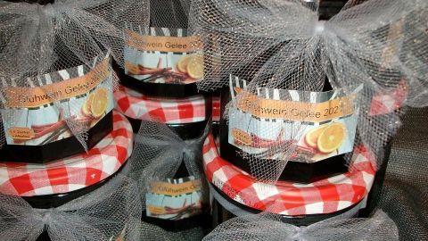 Mehrere Glühweingelee-Gläser mit karierten Deckeln stehen auf einem grauen Stoff, dekoriert mit Schleifen.