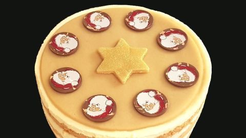 Eine Marzipandecke auf einer Torte zeigt festliche Schokoladenbilder von Weihnachtsmännern und einen goldenen Stern in der Mitte.