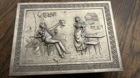 Eine verzierte Zinnbox liegt auf einem Holztisch, während sie mit Zahnpasta und einer Zahnbürste gereinigt wird.