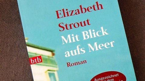 Ein Buchcover von Elizabeth Strout zeigt den Titel „Mit Blick aufs Meer“, umgeben von ruhigem, blauen Hintergrund.