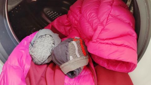 Eine leuchtend pinke Daunenjacke und Socken trocknen leise im Trockner, umgeben von der glatten Innenfläche der Trommel.